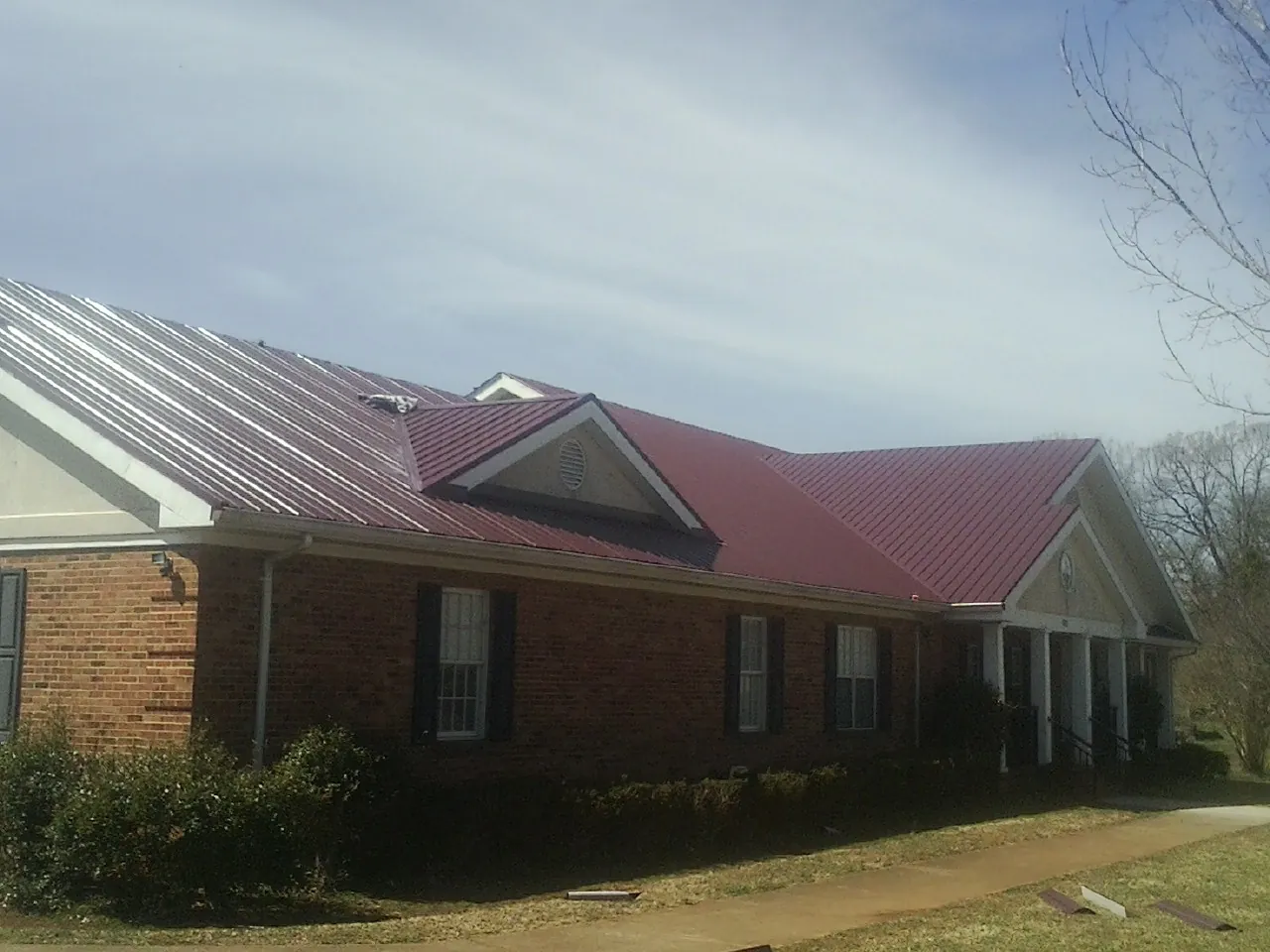 Red metal roof with gabled entries on a long brick building, from a Hail Damage Roof Repair job in Hancock